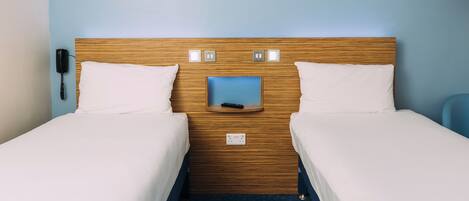 A hotel room with two single beds, a wooden headboard, a small bedside table, a phone, and a framed picture on the wall.