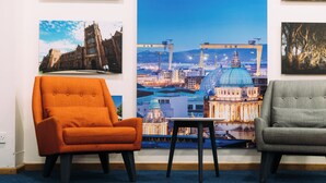 A room with two armchairs, a small table, and a large poster of a cityscape on the wall. - Travelodge Belfast Central (Belfast)
