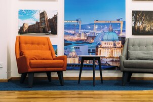 Une pièce comprenant deux fauteuils, une petite table et une grande affiche représentant un paysage urbain, accrochée au mur.