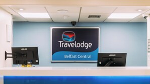 A reception desk with a 'Travelodge Belfast Central' sign, two monitors, and a 'welcome' message on the counter. - Travelodge Belfast Central (Belfast)
