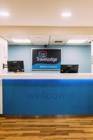 Un comptoir d'accueil avec une enseigne « Travelodge Belfast Central », deux écrans et un message de bienvenue.