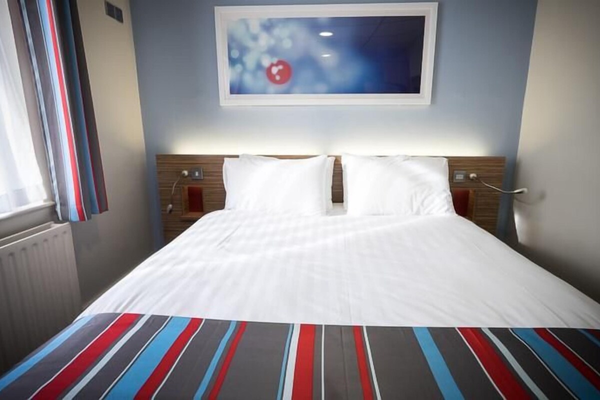 A neatly made bed with white linens in a hotel room.