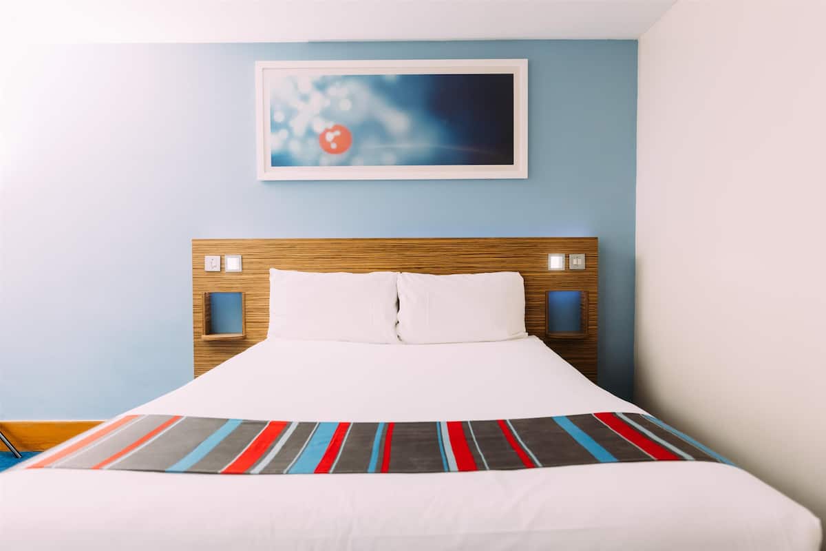 Un lit bien fait, avec une couverture à rayures, une tête de lit en bois et un tableau encadré accroché au mur.