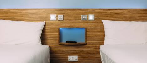 A hotel room with two beds, a wooden headboard, a television mounted on the wall, and a power outlet.