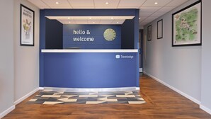 Un comptoir d’accueil avec une horloge, une pancarte indiquant « bonjour et bienvenue » et le logo de Travelodge.