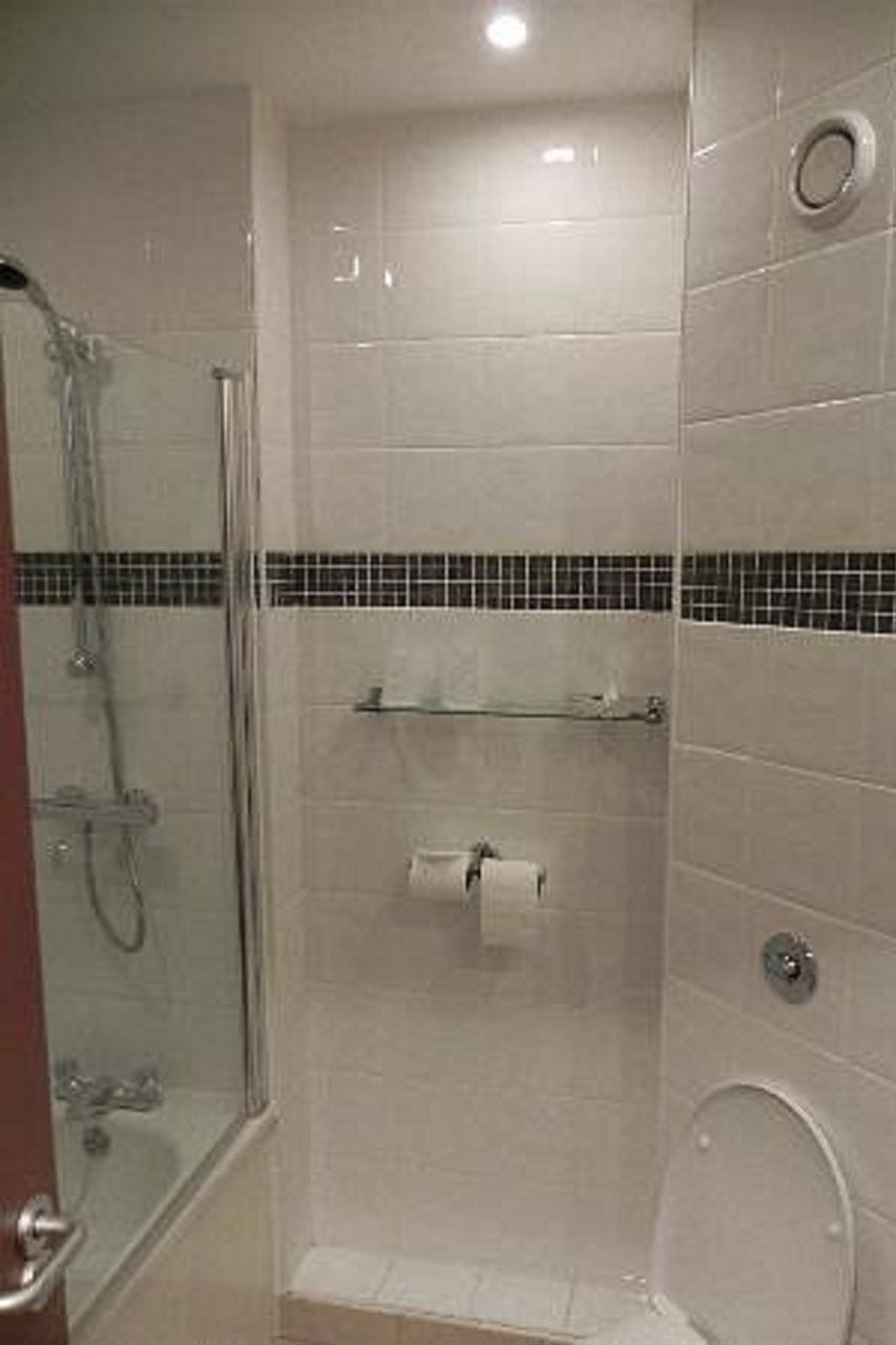 Kylpyhuoneessa on lasiseinällä varustettu suihku, wc ja hylly, jossa on hygieniatuotteita.