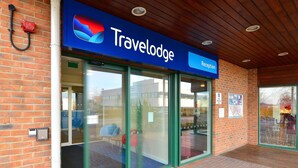 Entrada de um hotel Travelodge, com balcão de recepção, portas de vidro e fachada de tijolos.