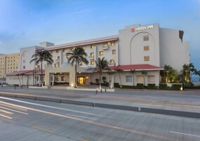 Um hotel com fachada moderna, várias varandas e palmeiras.