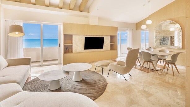 Una sala de estar moderna con un televisor grande, asientos cómodos, un comedor y vistas al mar.
