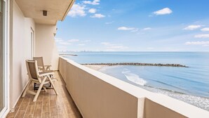 Un balcón con vista al mar, una silla y una mesa.