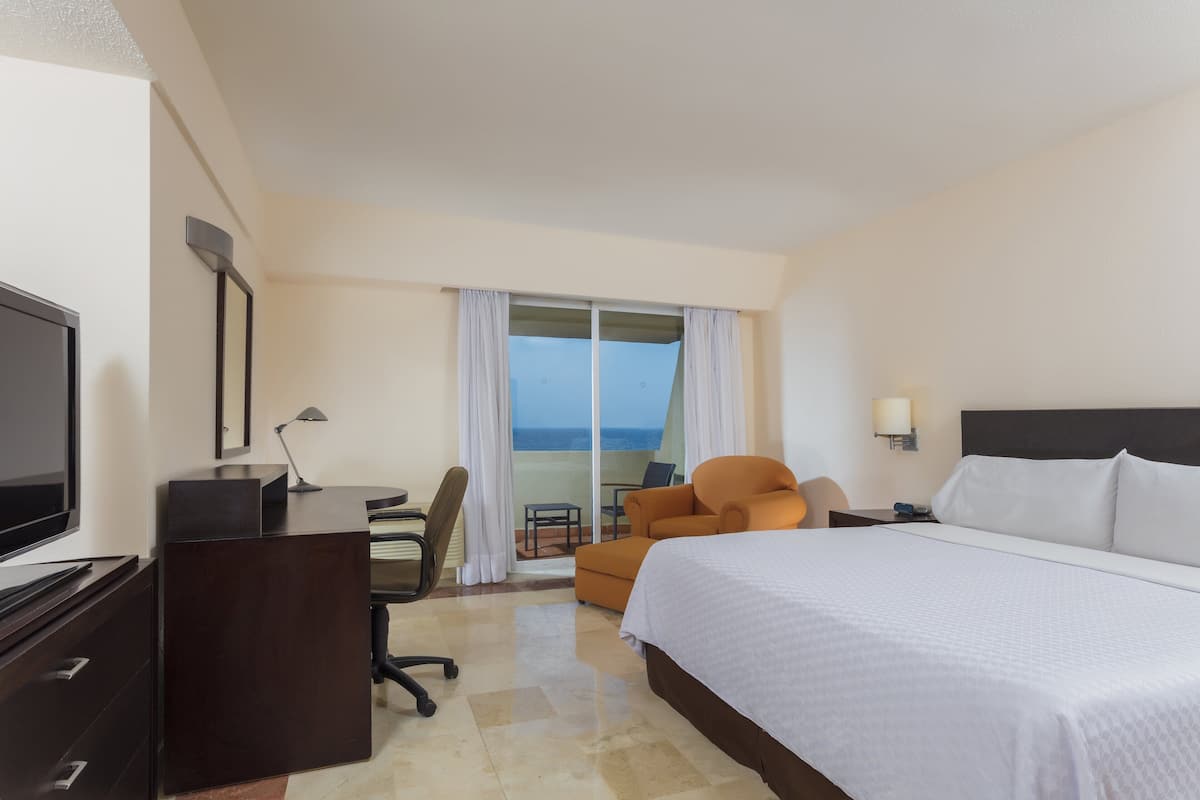 Una habitació d'hotel amb un llit, una taula, una cadira, un televisor i vista a l'oceà.
