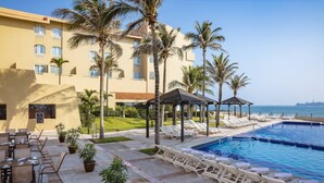 Un área junto a la piscina con sillones de descanso, una piscina pequeña y un edificio con varias ventanas y balcones.