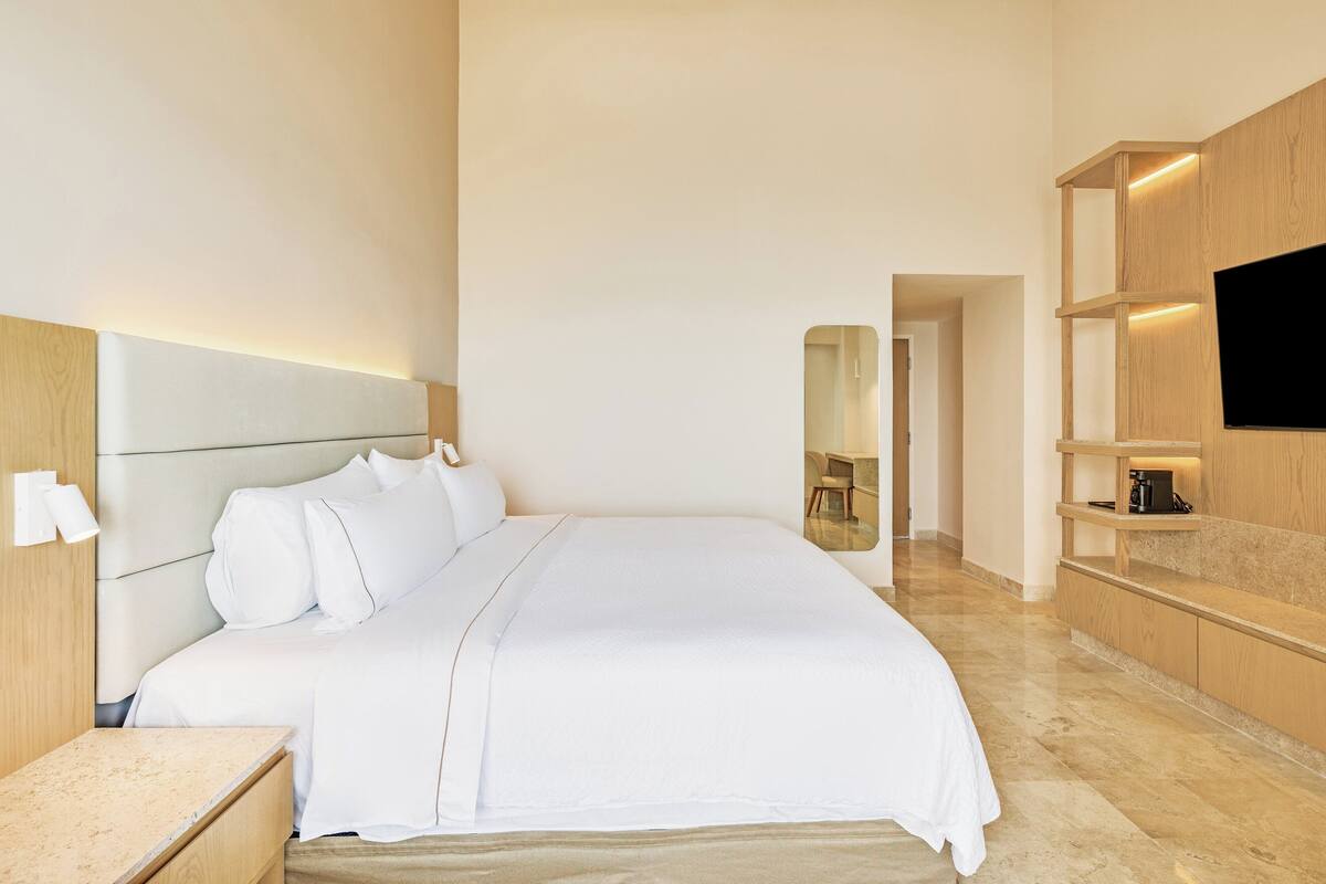 Habitació d'hotel moderna amb un llit gran, una televisió de pantalla plana penjada a una paret de fusta i una petita zona de seients amb taula i cadires.