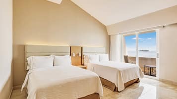 A hotel room with two beds, a large window with a view, and a balcony with a table and chairs.