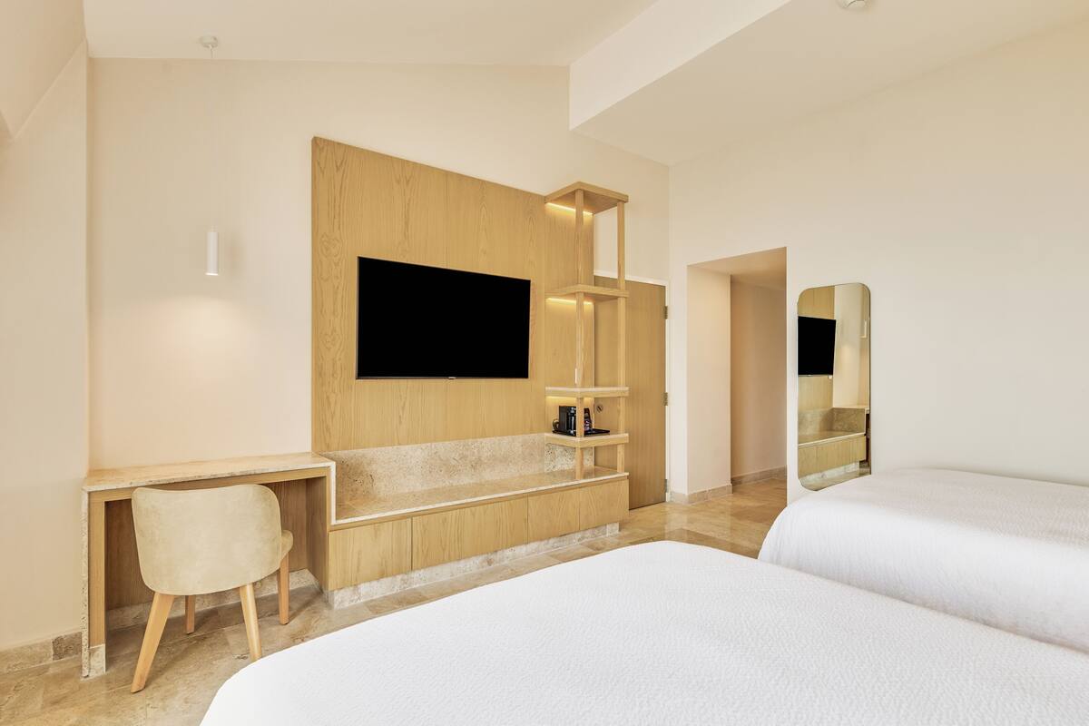 Habitació d'hotel moderna amb escriptori de fusta, televisió de pantalla plana, mirall i dos llits.