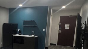 A small room with a kitchenette, a dark-colored refrigerator, a sink, and a door with a lock. - Studio 6 Oklahoma City - Moore/Norman (Oklahoma City)