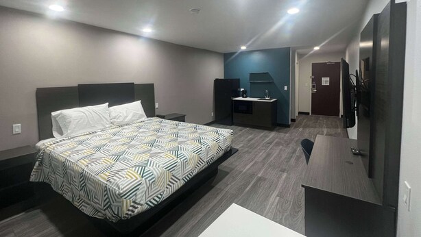 A modern hotel room with a large bed, a desk, a kitchenette, and a TV. - Studio 6 Oklahoma City - Moore/Norman (Oklahoma City)
