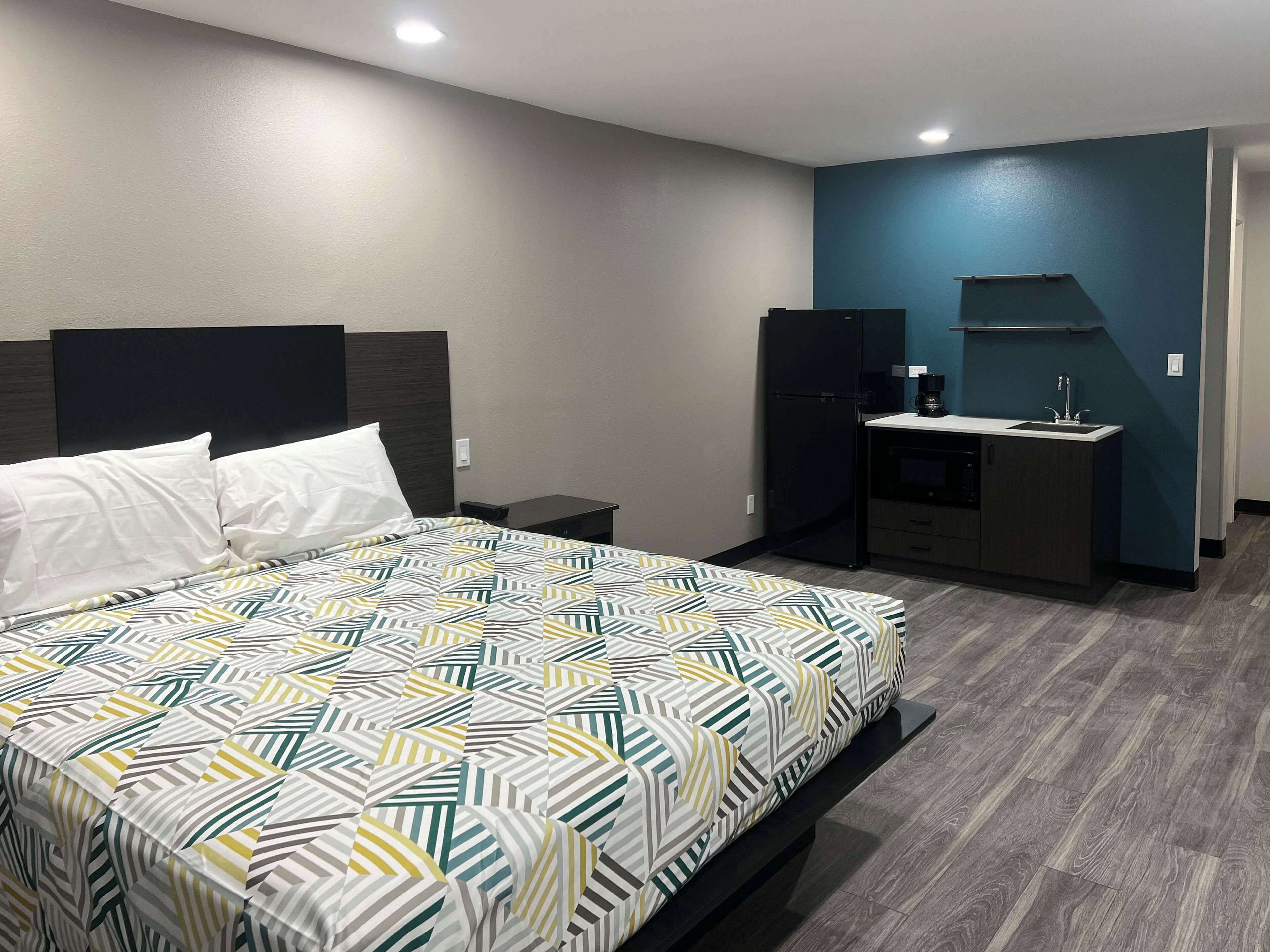 A hotel room with a bed, a small desk with a refrigerator, a coffee maker, and a sink.