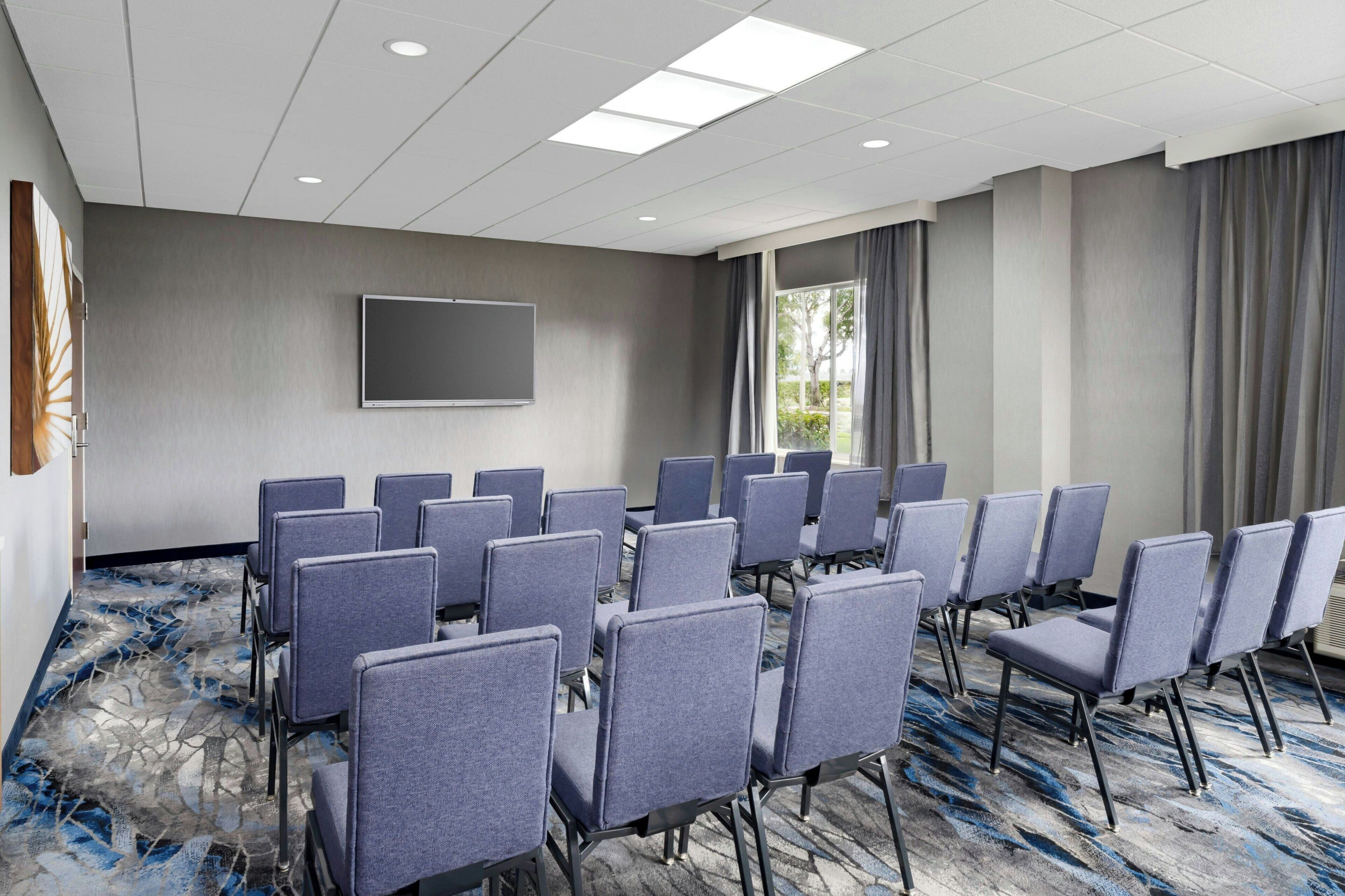 A conference room with rows of chairs, a large flat-screen TV, and a patterned carpet.