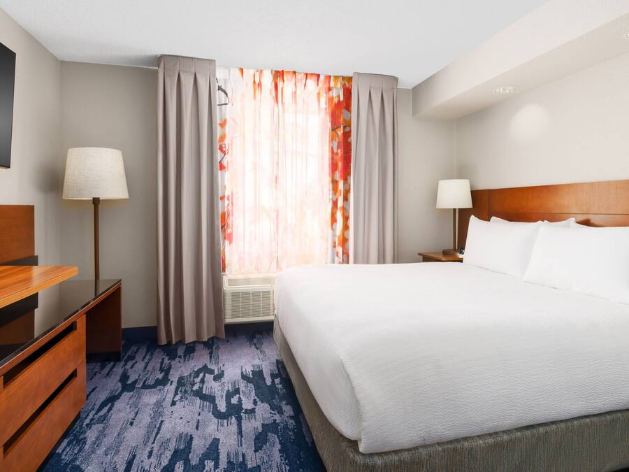 Une chambre d’hôtel avec un grand lit, un bureau, une chaise, une lampe et une fenêtre avec des rideaux.