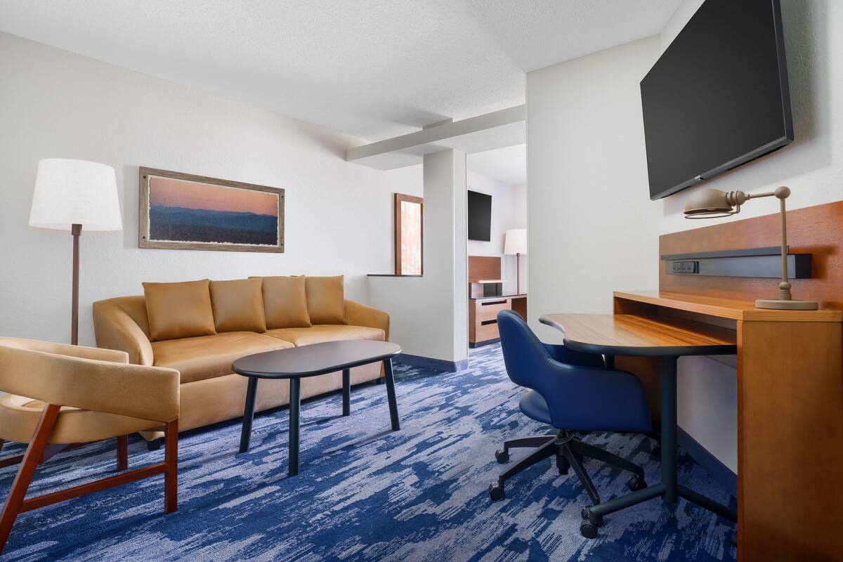 Habitación de hotel con sofá, escritorio, silla, televisión y un cuadro en la pared.