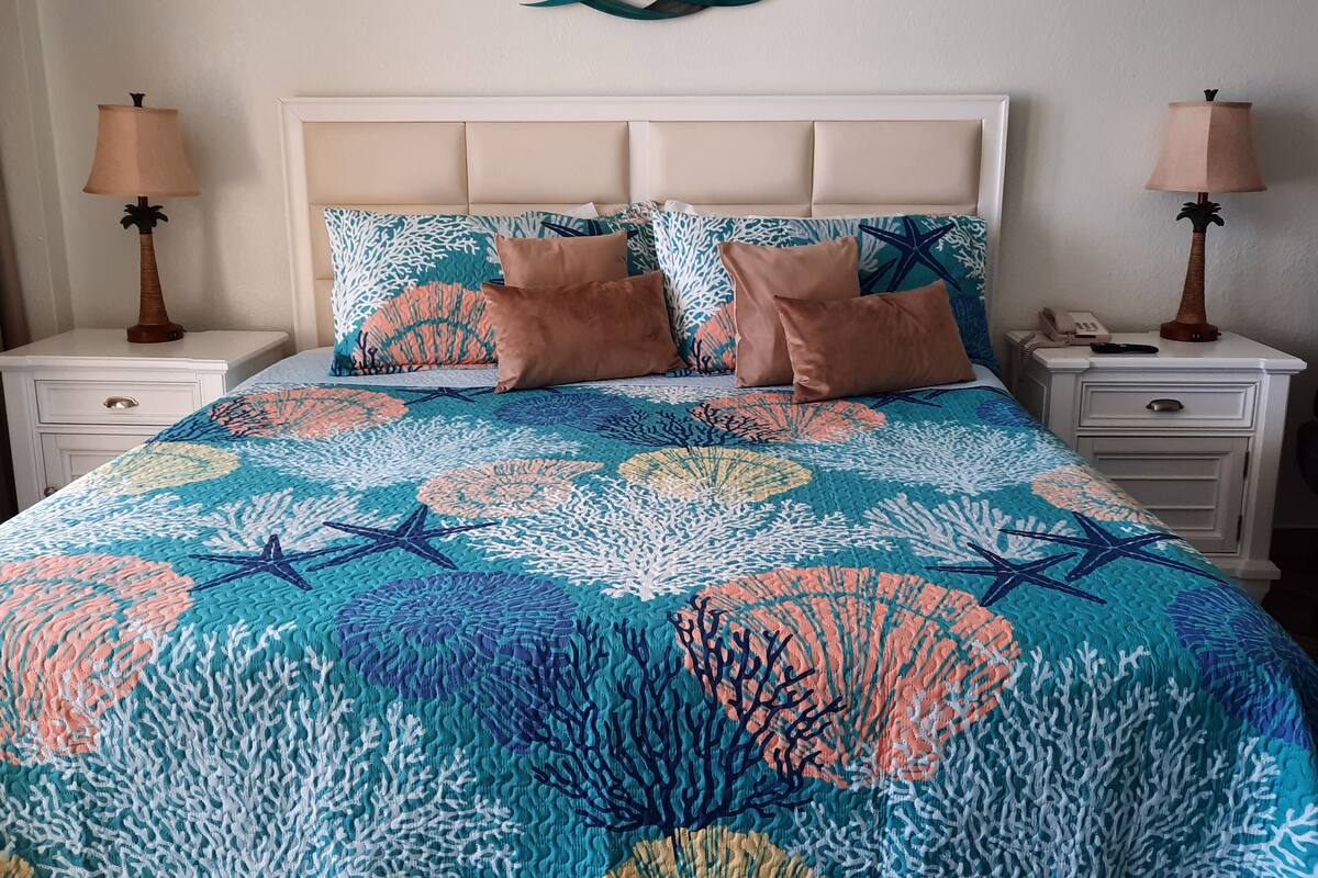 A bed with a floral-patterned bedspread, two nightstands with lamps, and a decorative wall piece above the bed.