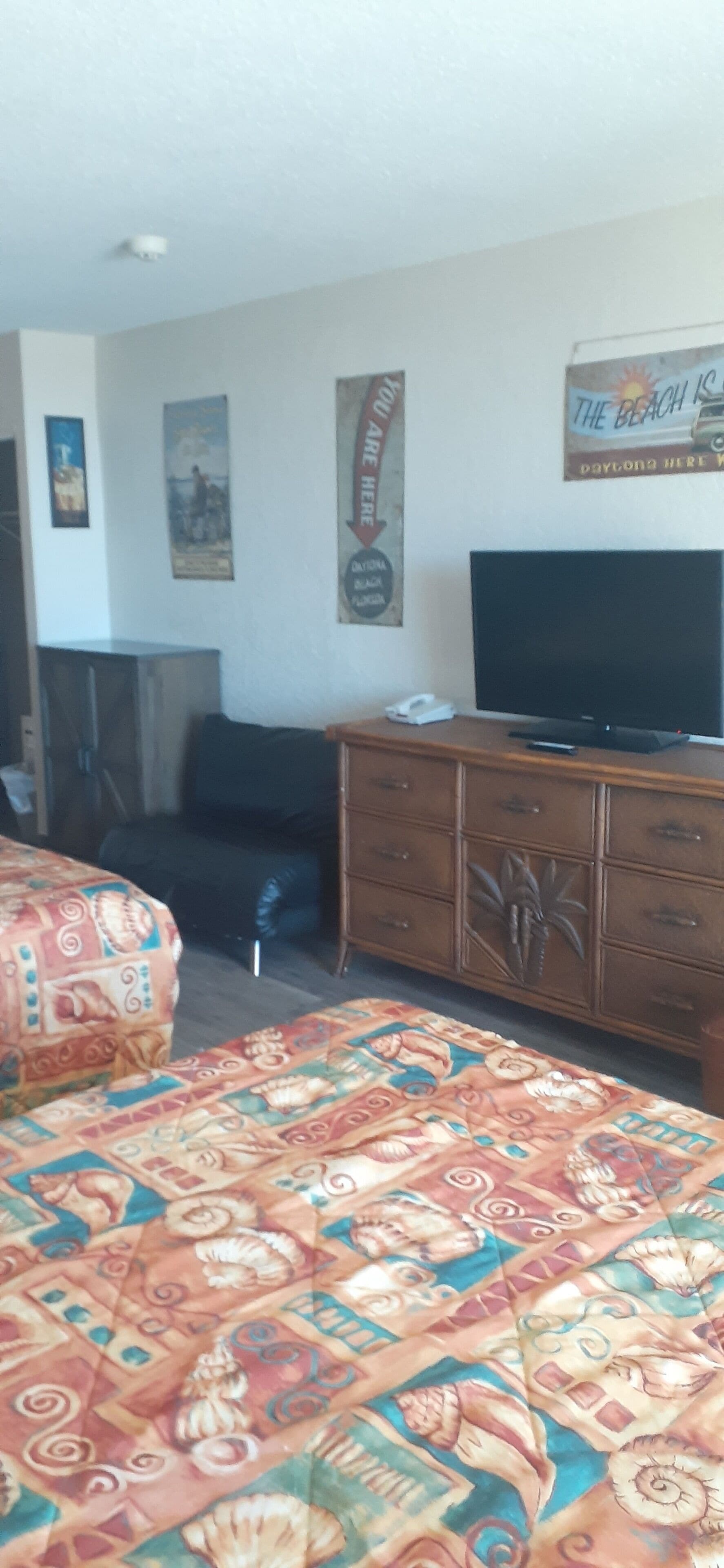 A hotel room with a bed, a television, a dresser, and a poster on the wall.