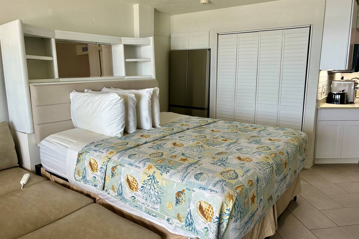 A bedroom with a bed, a sofa, a wardrobe, and a kitchenette.