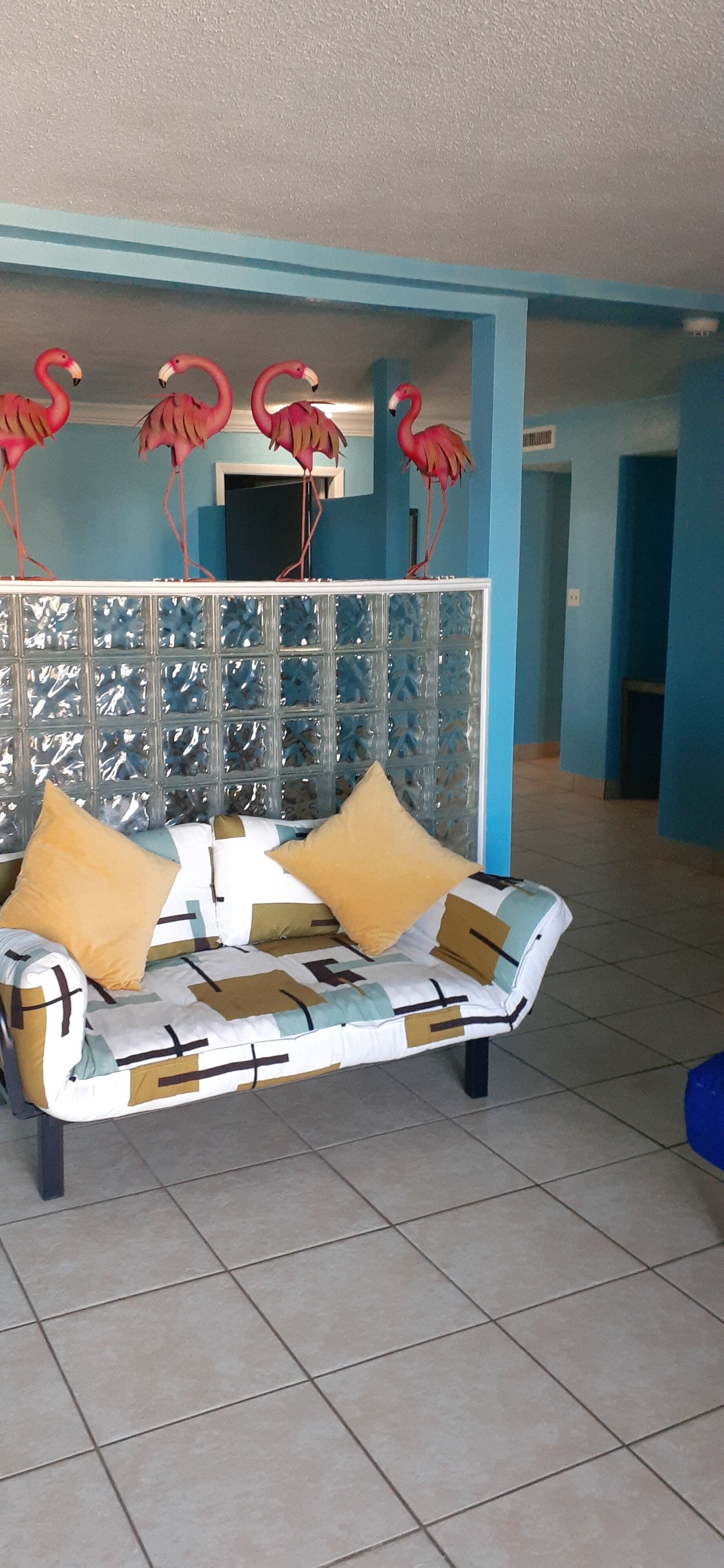 Quarto com sofá estampado, parede decorativa com painel de vidro e luminária no teto.