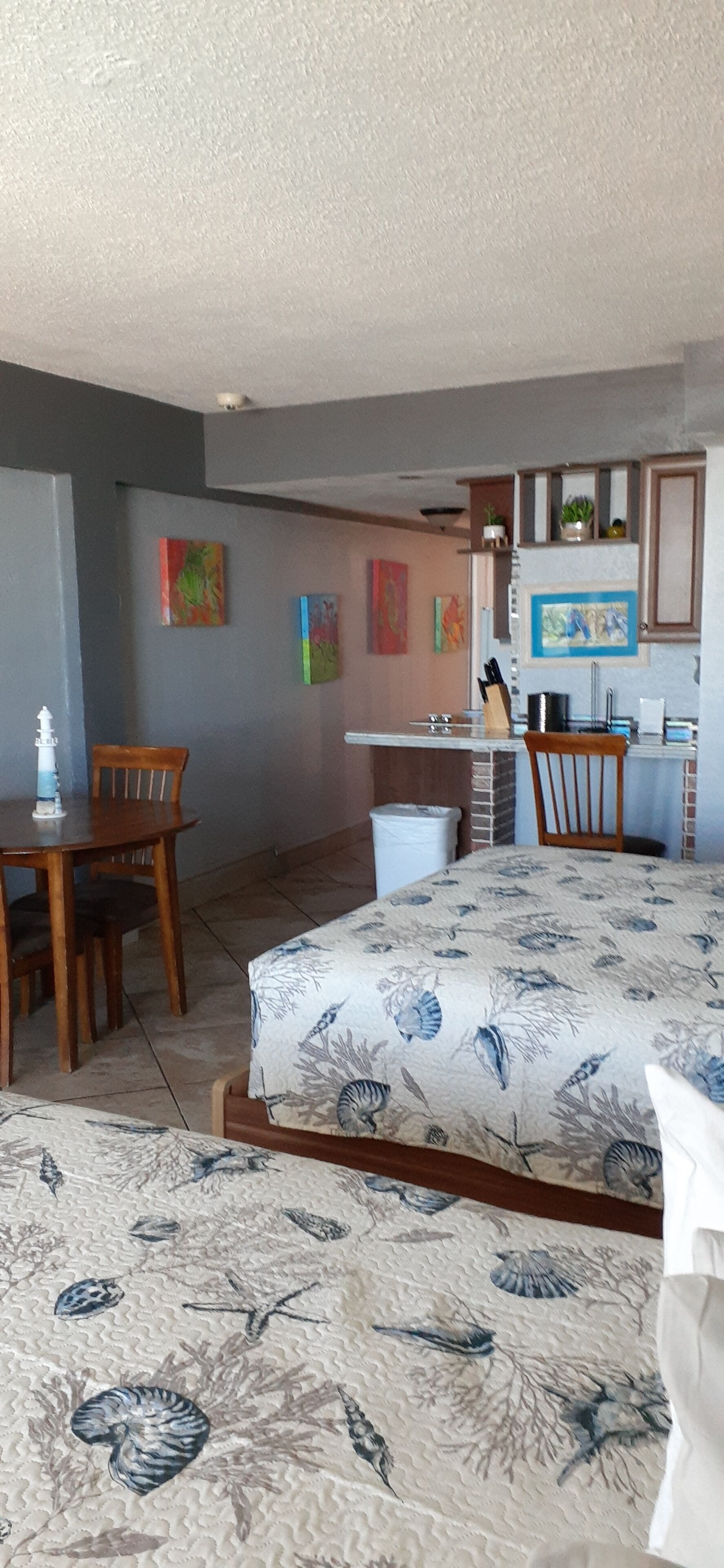 A room with a bed, a dining table, and chairs. There is a kitchen area with cabinets and a sink.
