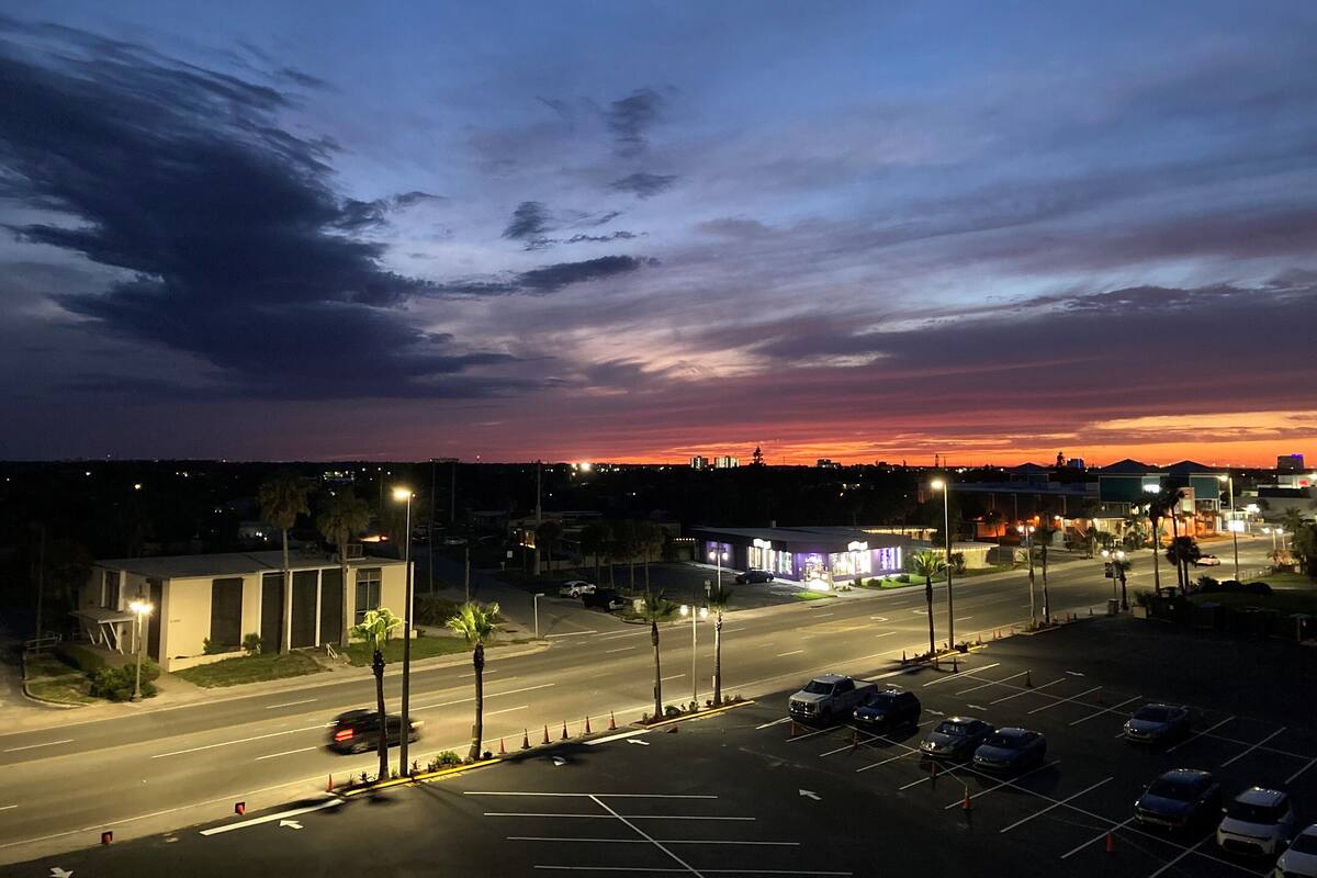 A parking lot with multiple cars and a building with illuminated signage in the background.