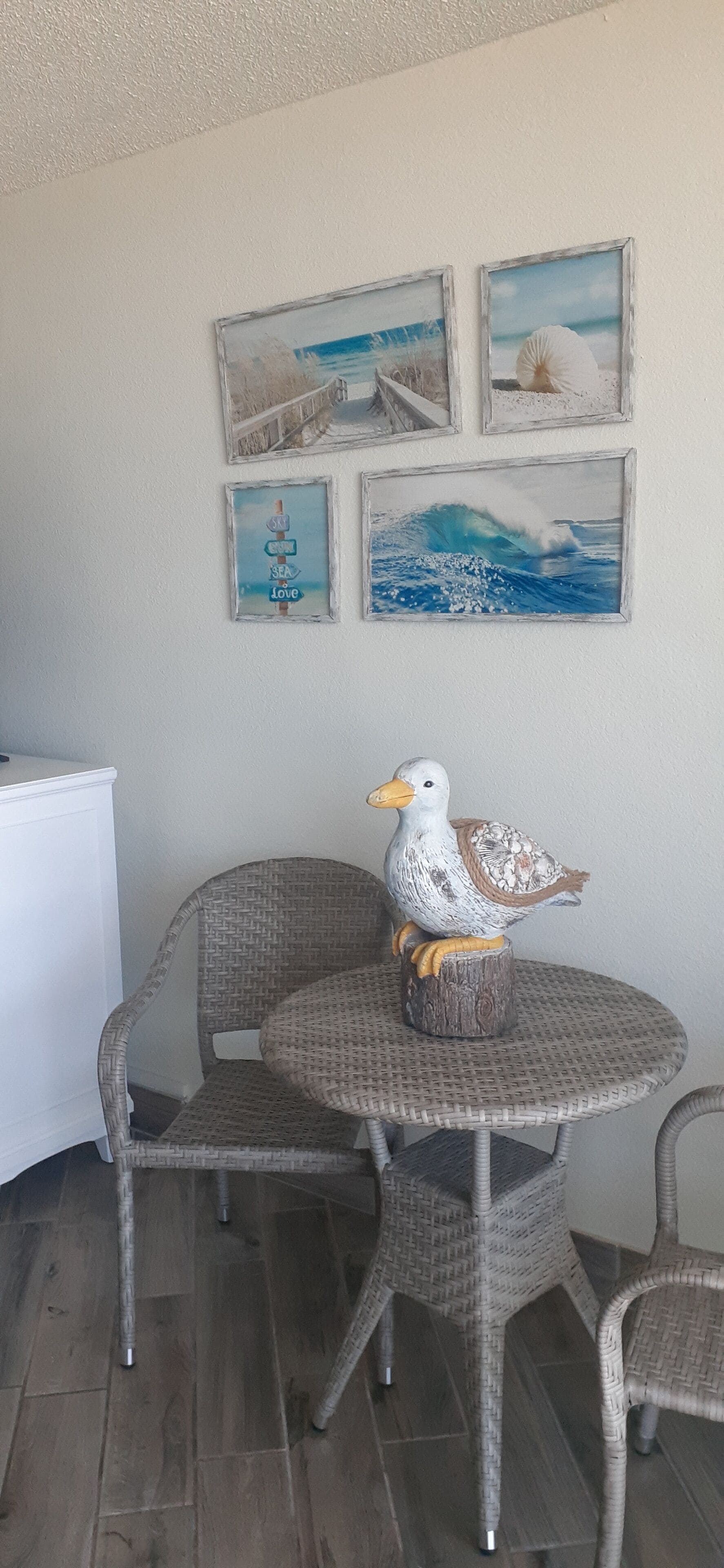 Een eetgedeelte met rieten stoelen en een ronde tafel, een decoratief beeld van een vogel, en lijstwerken aan de wand.