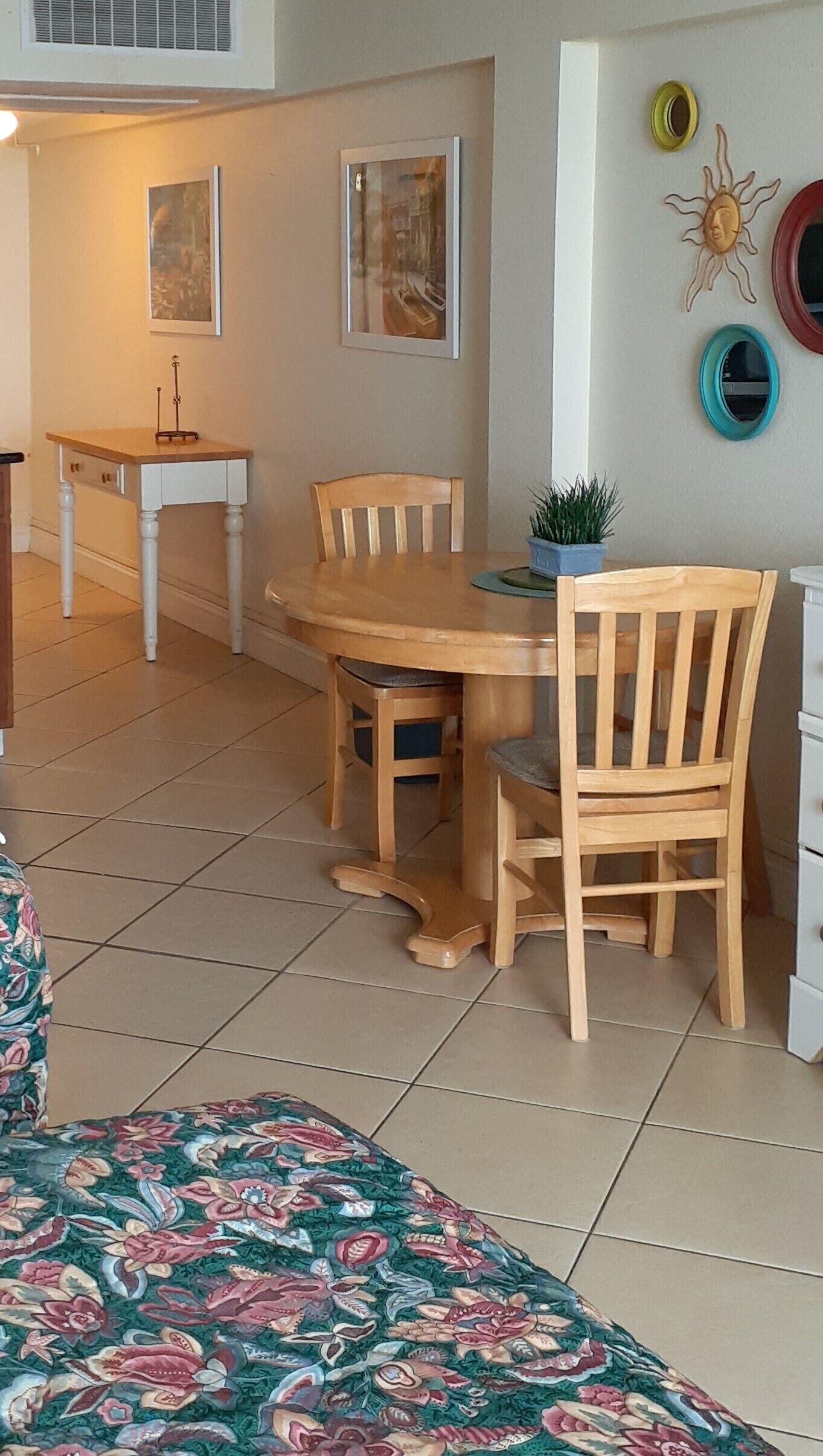 A dining area with a wooden table and chairs, a small potted plant, and artwork on the walls.