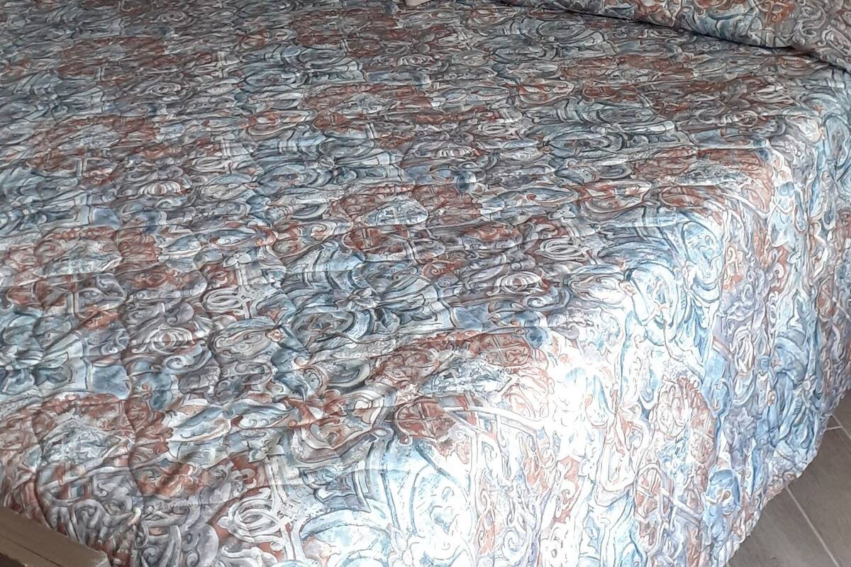A bed with a patterned bedspread, a wooden headboard, and a painting of a beach scene on the wall.
