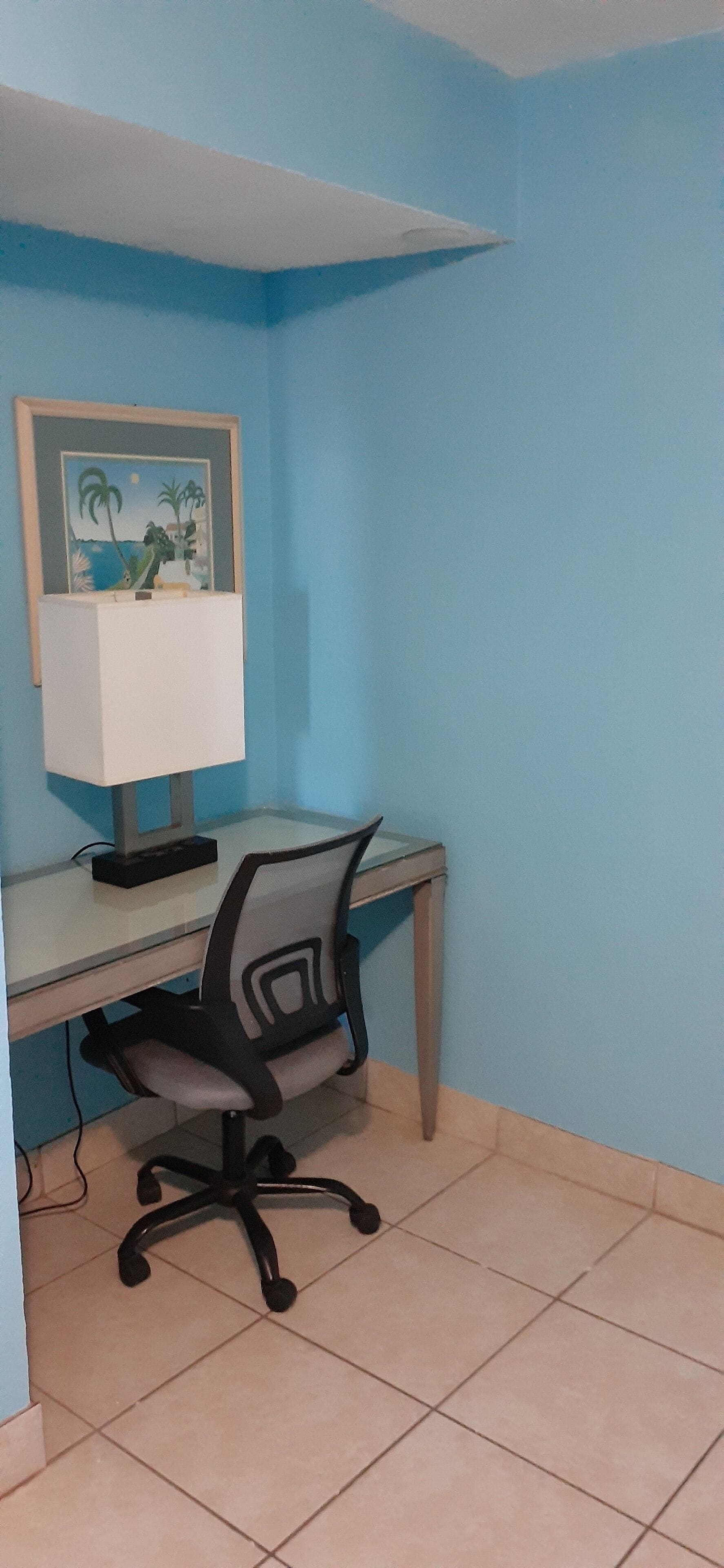 A room with a desk, chair, and a framed picture on the wall.