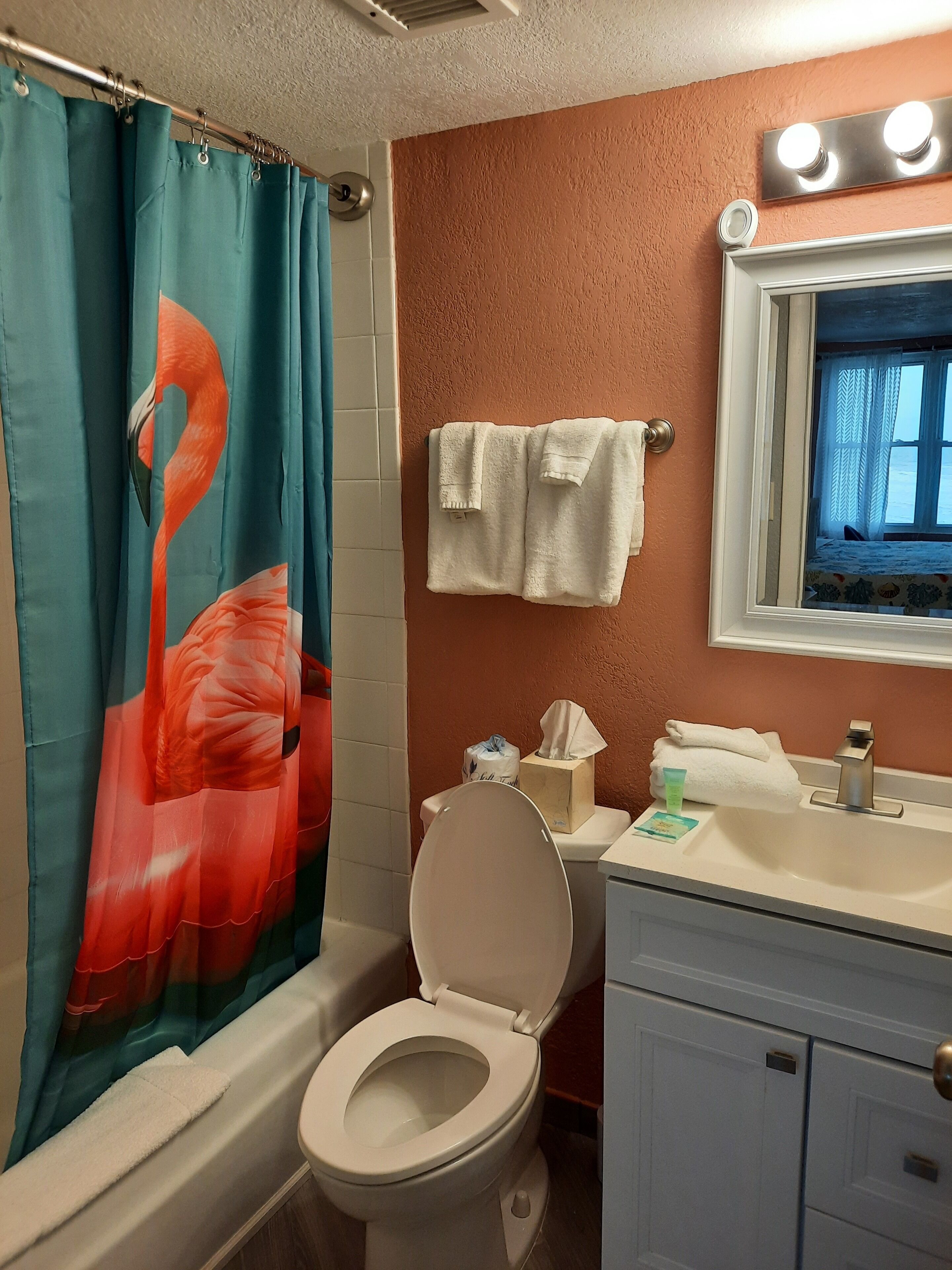 A bathroom with a toilet, sink, and mirror. There is a towel rack with towels and a tissue box.