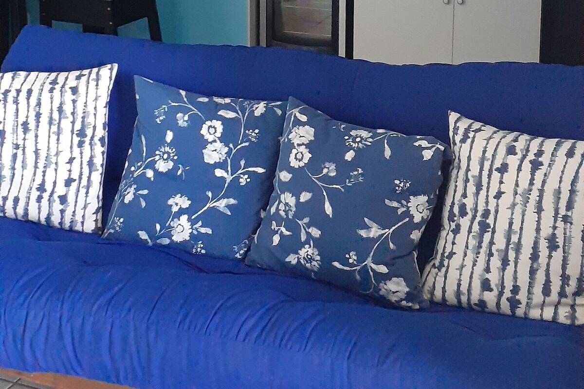 A blue sofa with floral cushions in a room with a kitchen area.