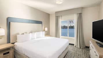 A hotel room with a large bed, a TV, a desk, and a window with a view of the sea.