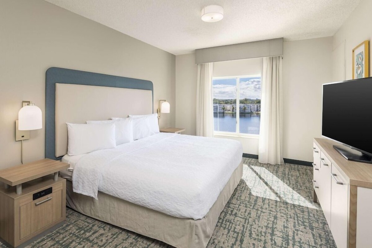 Habitación de hotel con una cama grande, televisión, escritorio y ventana con vista a un cuerpo de agua.