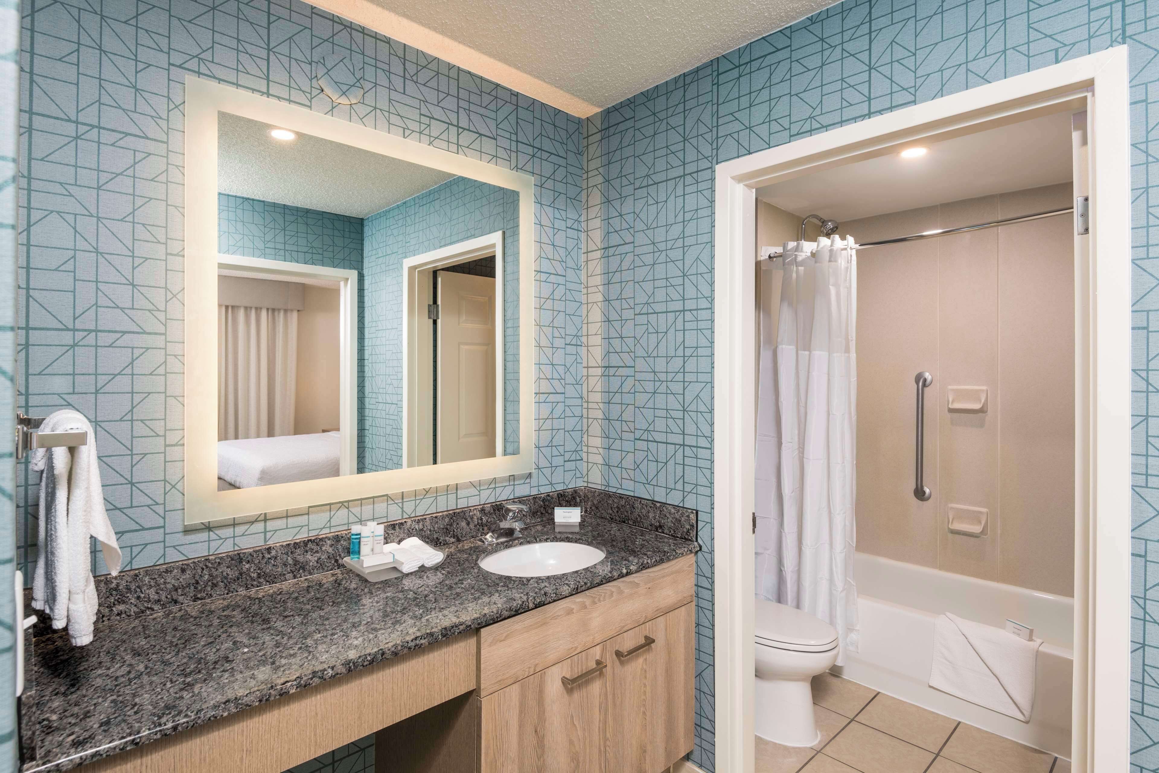 Un baño con encimera de granito, un lavabo blanco, un espejo y zona de ducha.