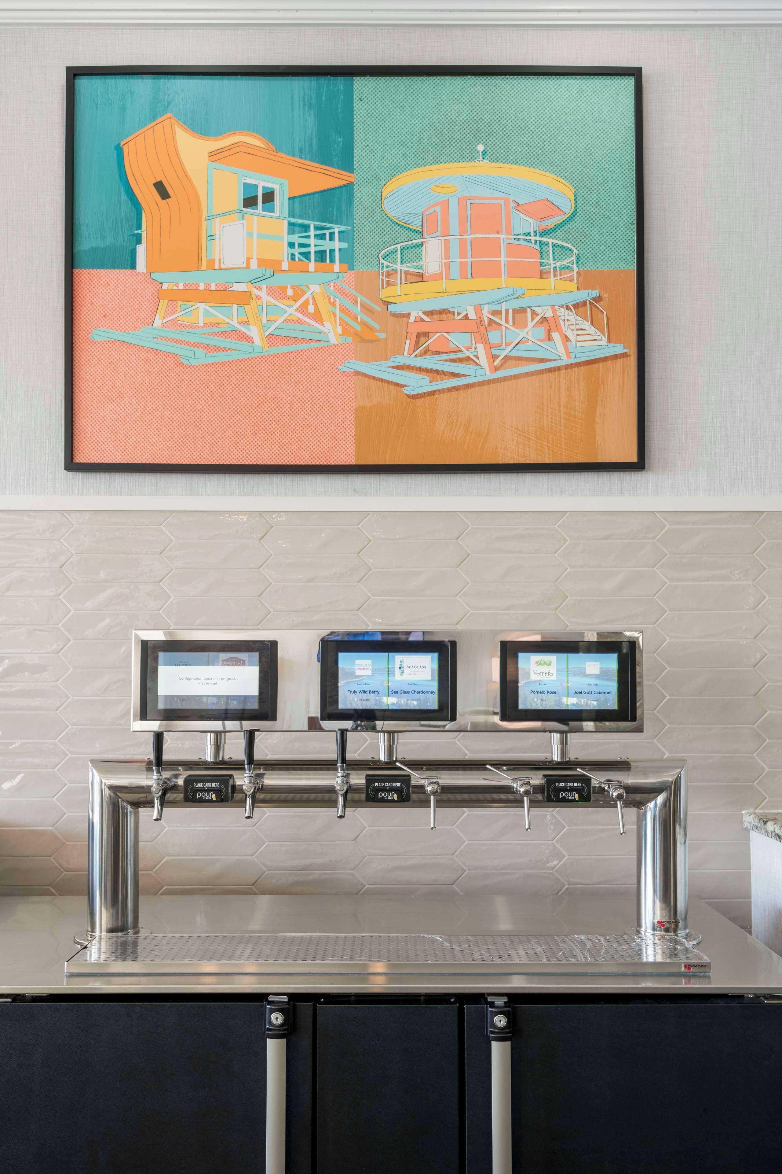 Una zona de bar moderna amb una pantalla digital que mostra el menú, un dispensador d'aigua i una obra d'art emmarcada penjada a la paret.
