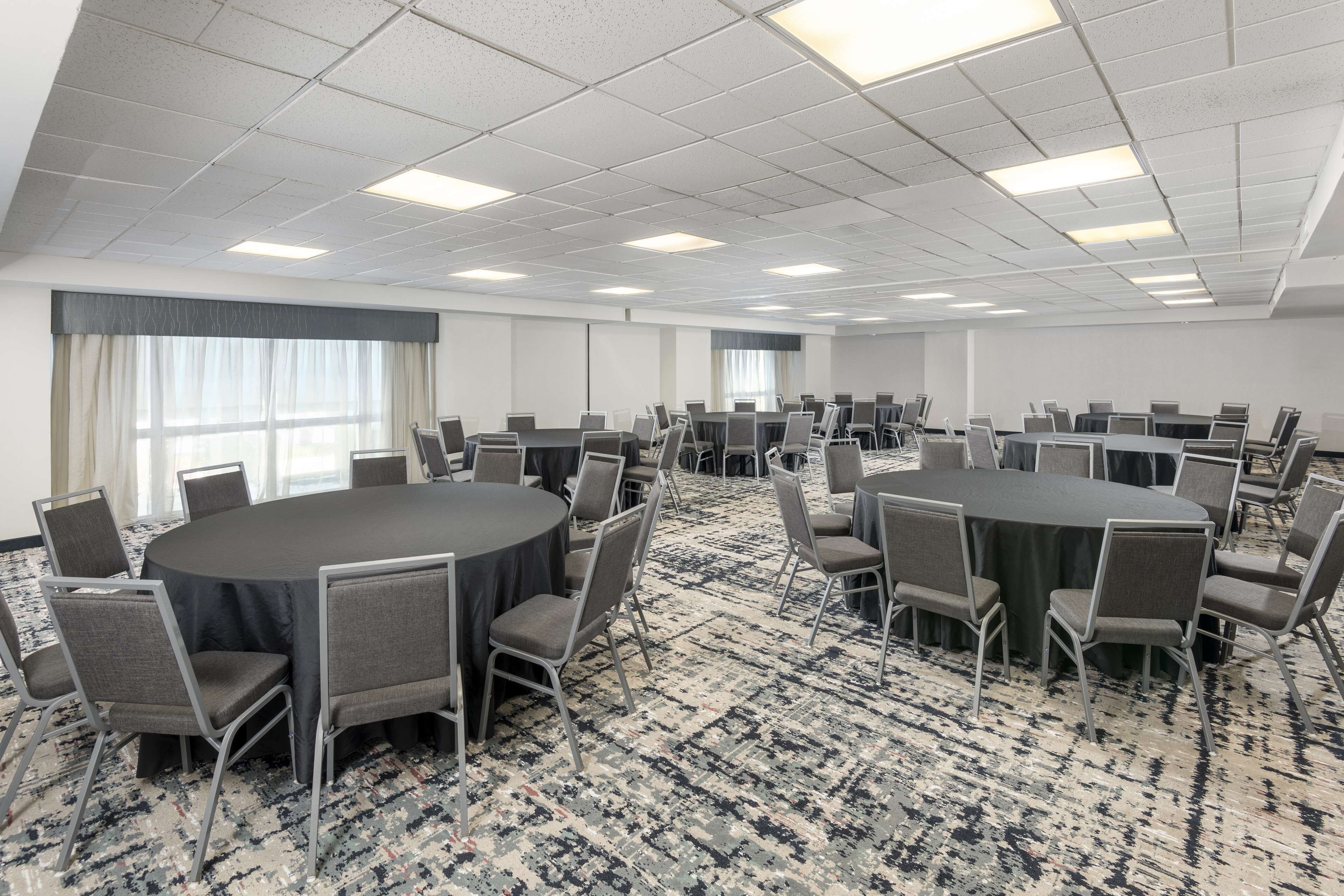 A conference room with a large round table surrounded by chairs, carpeted flooring, and a ceiling with fluorescent lights.