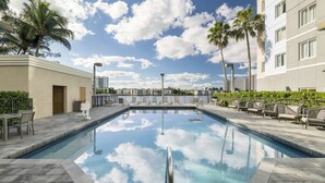 A swimming pool with a clear view of the sky and clouds, surrounded by lounge chairs and palm trees.