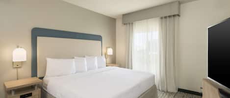 Habitación de hotel con una cama grande, mesitas de noche, un televisor de pantalla plana y una ventana con cortinas.