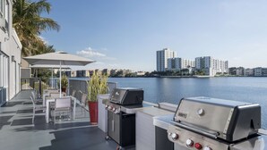 A rooftop patio with a grill, outdoor seating, and a view of the city skyline over water.