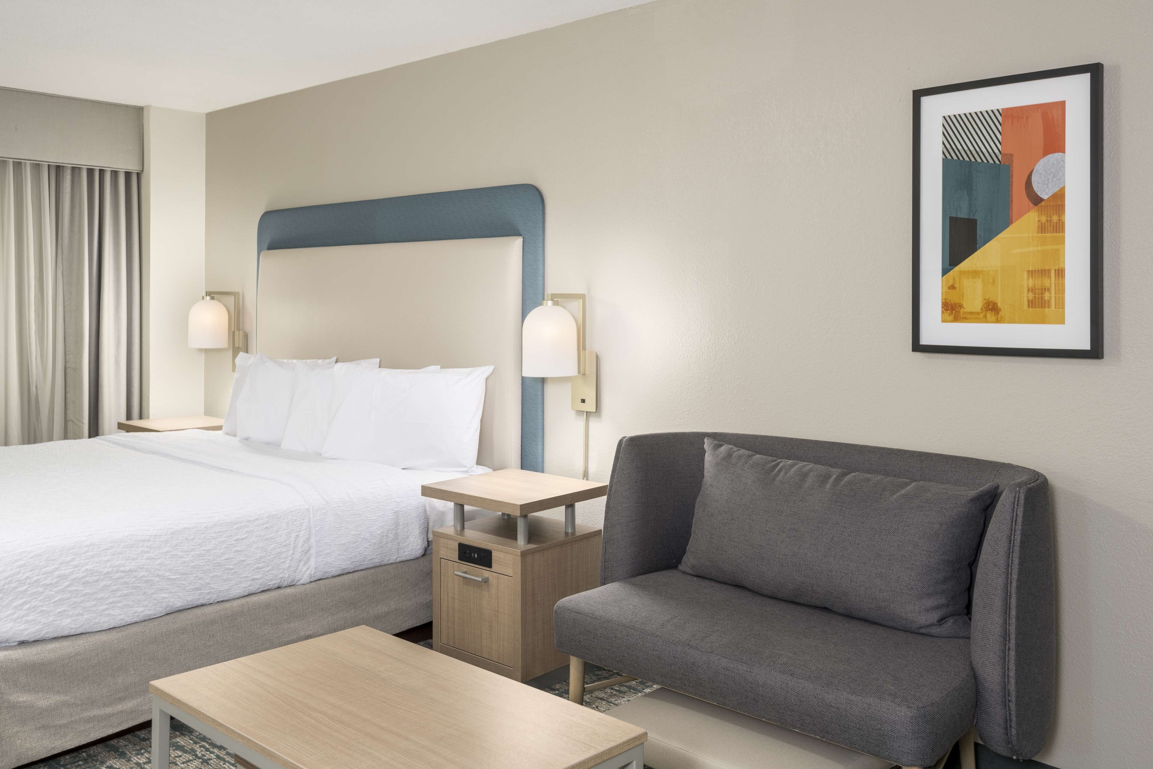 A hotel room with a bed, a sofa, a nightstand, and a framed picture on the wall.