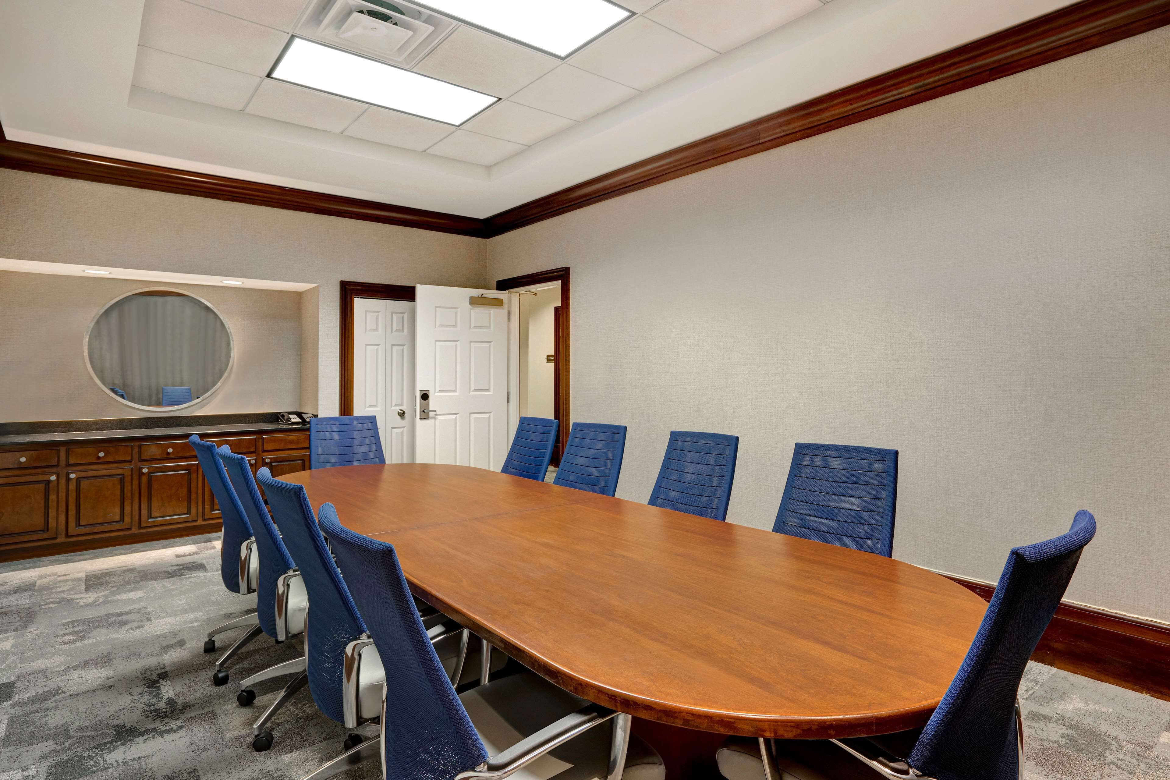 A conference room with a wooden table, blue chairs, a round mirror, and a carpeted floor.