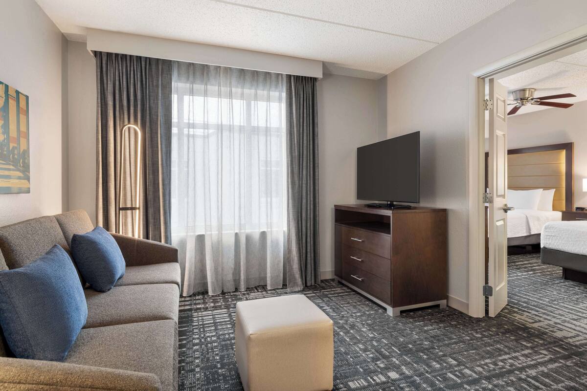 A hotel room with a sofa, ottoman, TV, and a bed.