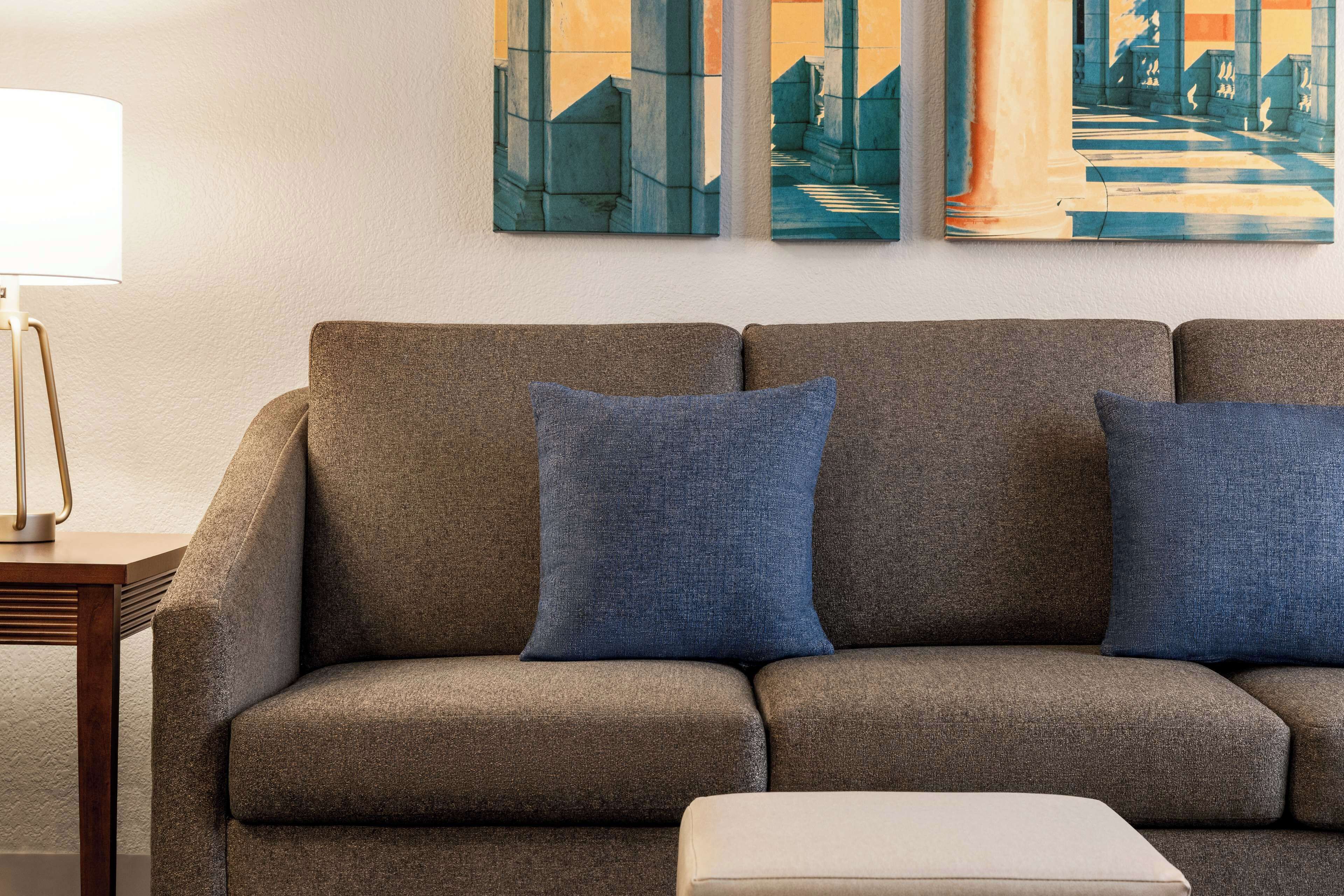 A modern living room with a sofa, two blue cushions, and a small table with a lamp.