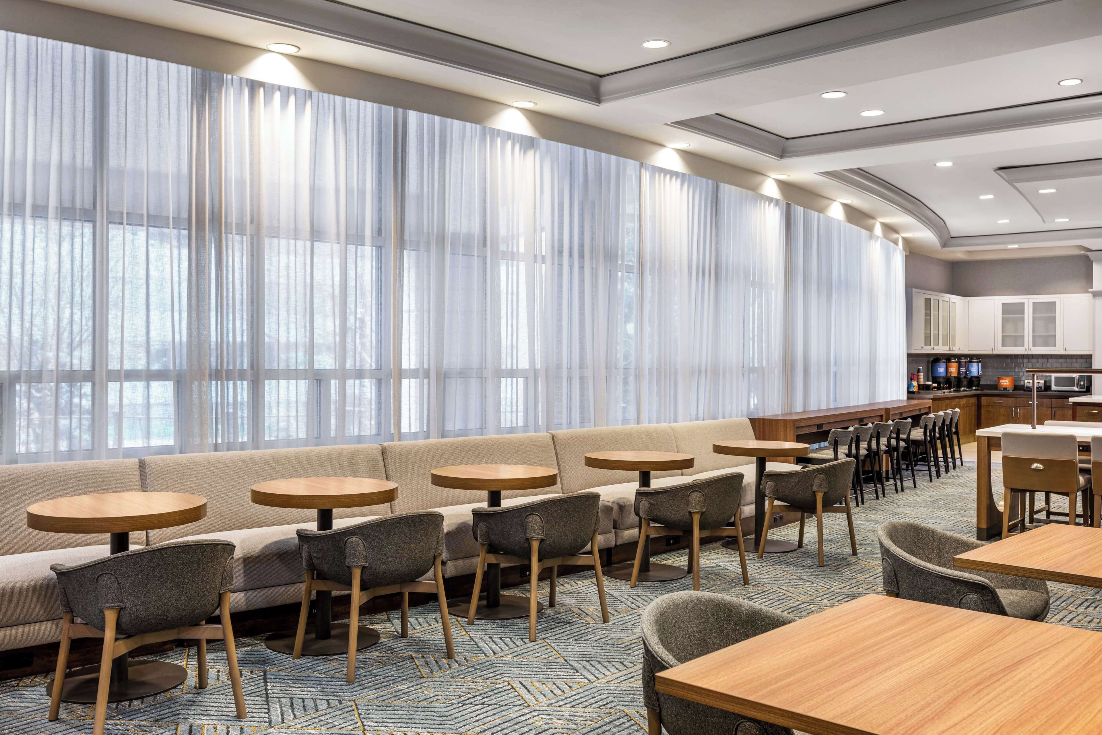 A modern hotel lobby with a seating area, large windows, and a kitchenette.